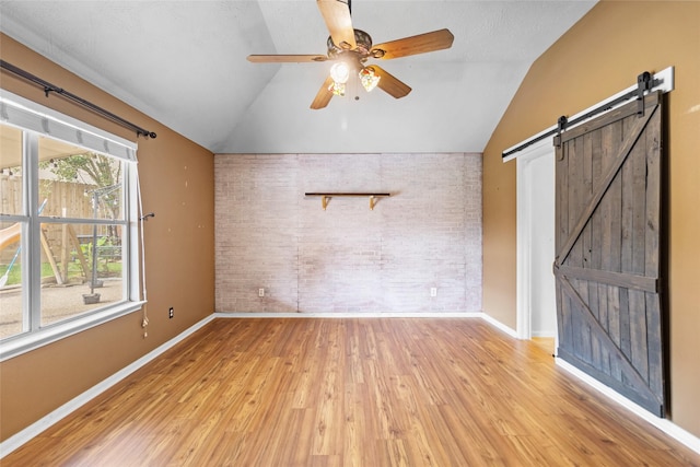 interior space featuring lofted ceiling, brick wall, baseboards, a barn door, and a ceiling fan
