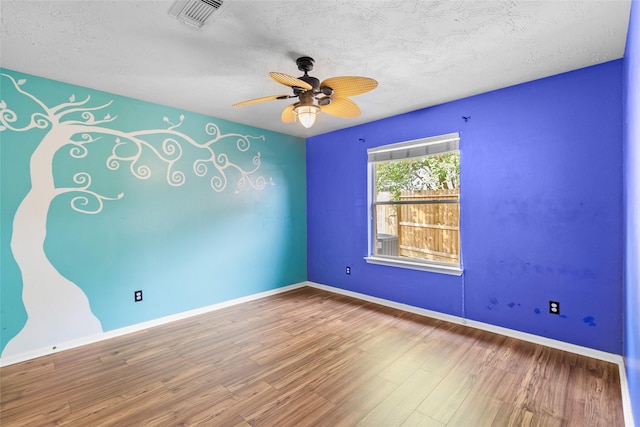 empty room with a ceiling fan, a textured ceiling, visible vents, wood finished floors, and baseboards