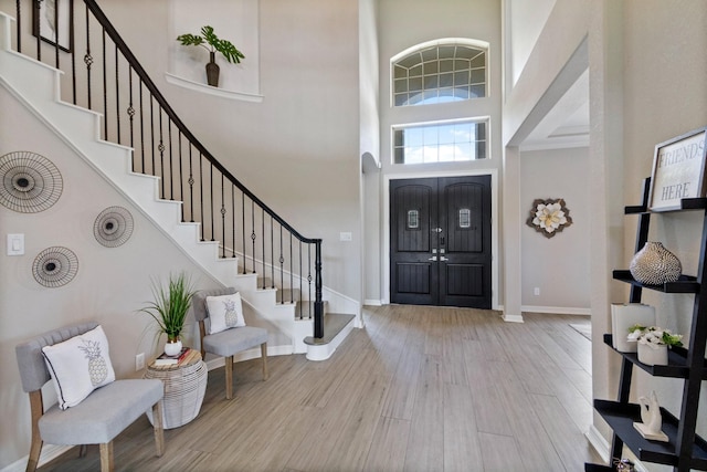 foyer entrance with stairway, baseboards, wood finished floors, and a towering ceiling