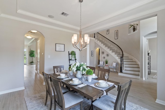 dining space featuring crown molding, arched walkways, light wood-style flooring, stairs, and visible vents