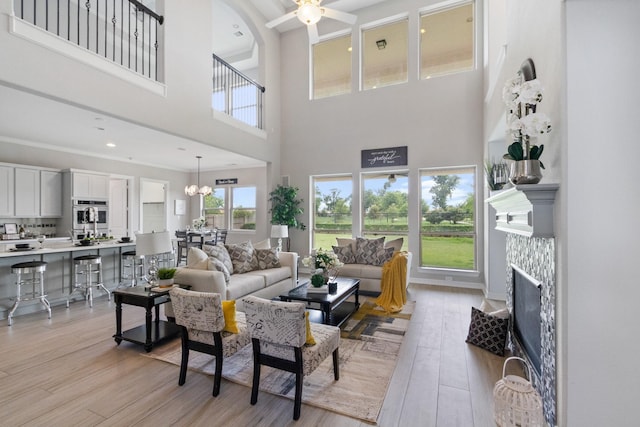 living room with a fireplace, a towering ceiling, ceiling fan with notable chandelier, and light wood-style floors