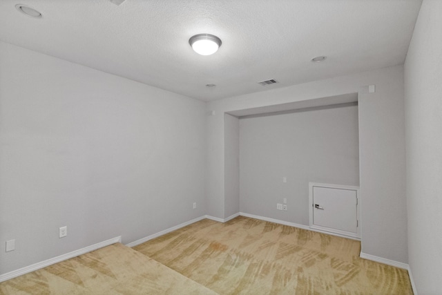 spare room with light colored carpet, a textured ceiling, baseboards, and visible vents