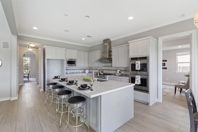 kitchen featuring wall chimney range hood, arched walkways, white cabinets, a sink, and stainless steel appliances