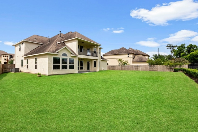 back of property featuring a balcony, a fenced backyard, stucco siding, a lawn, and central air condition unit