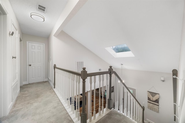 hallway featuring visible vents, carpet, vaulted ceiling with skylight, and an upstairs landing