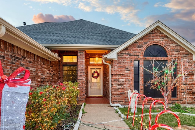 view of exterior entry with brick siding and a shingled roof