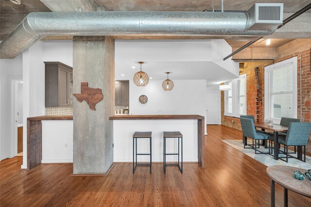204 Travis St Unit 4A, Houston, TX 77002 - kitchen featuring brick wall, visible vents, hanging light fixtures, tasteful backsplash, and wood finished floors