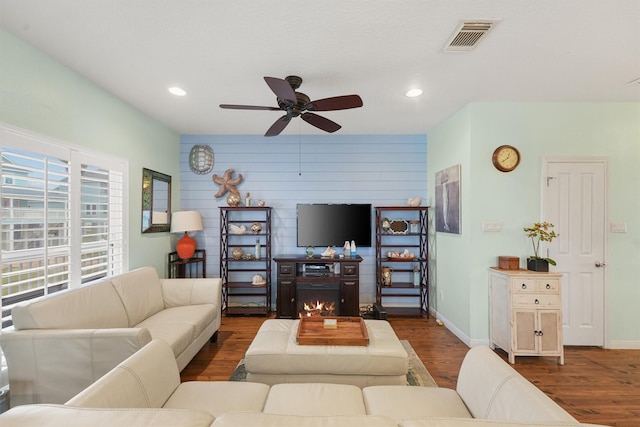 living room with visible vents, wood finished floors, ceiling fan, a warm lit fireplace, and recessed lighting