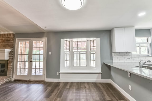 unfurnished dining area featuring a brick fireplace, baseboards, a sink, and dark wood-type flooring