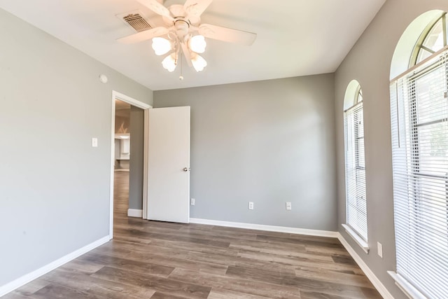 empty room with baseboards, ceiling fan, wood finished floors, and visible vents