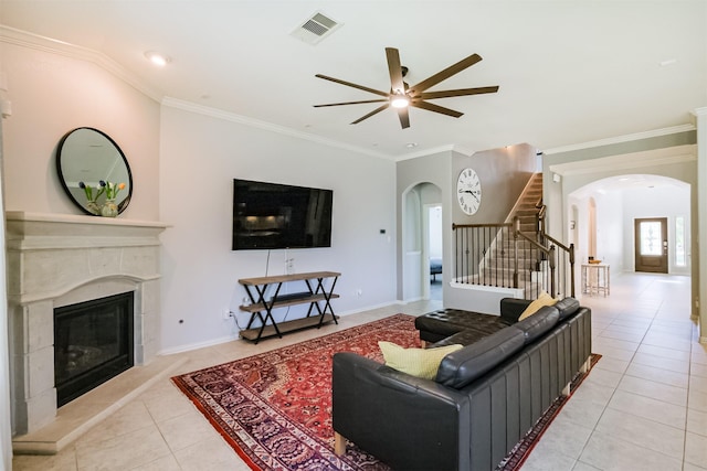 living room featuring a ceiling fan, arched walkways, light tile patterned floors, stairway, and a premium fireplace