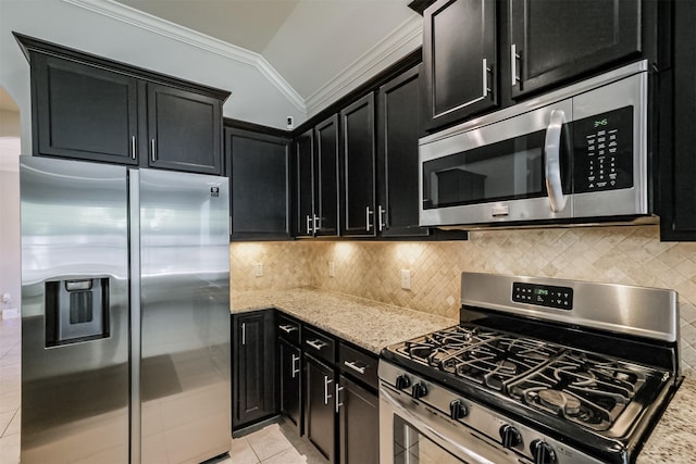 kitchen featuring crown molding, appliances with stainless steel finishes, light stone counters, dark cabinetry, and vaulted ceiling