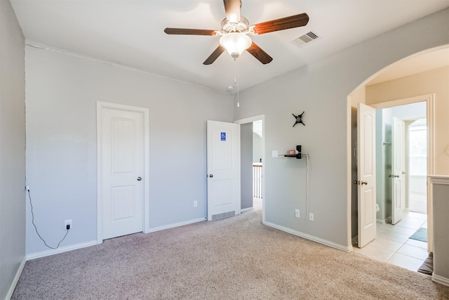 unfurnished bedroom with visible vents, arched walkways, baseboards, and light carpet