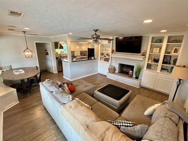 living area with ceiling fan, a fireplace, ornamental molding, visible vents, and dark wood-style floors