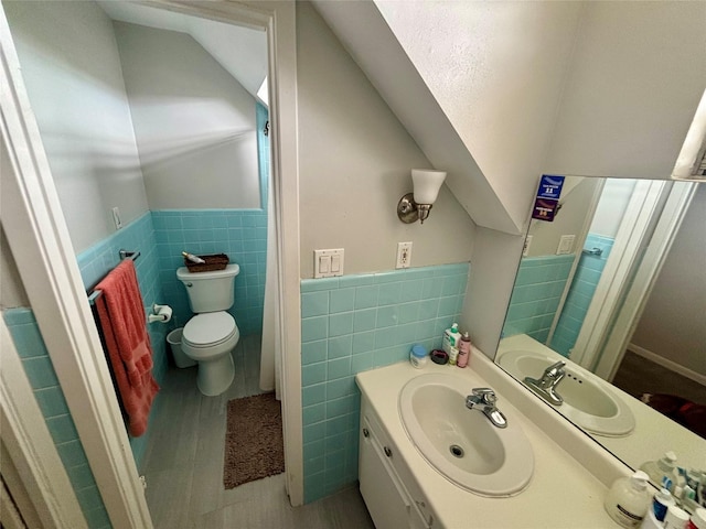 bathroom featuring vanity, wood finished floors, lofted ceiling, toilet, and tile walls