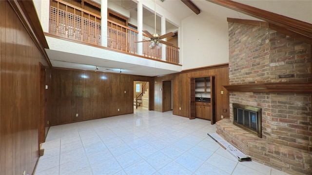unfurnished living room featuring a ceiling fan, a fireplace, stairway, high vaulted ceiling, and wooden walls