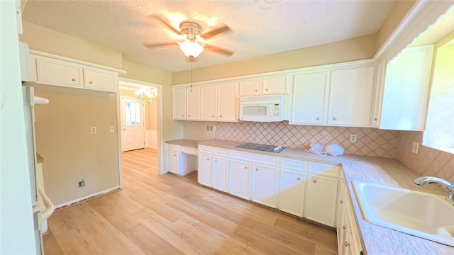 kitchen with a sink, white microwave, white cabinetry, and black electric cooktop