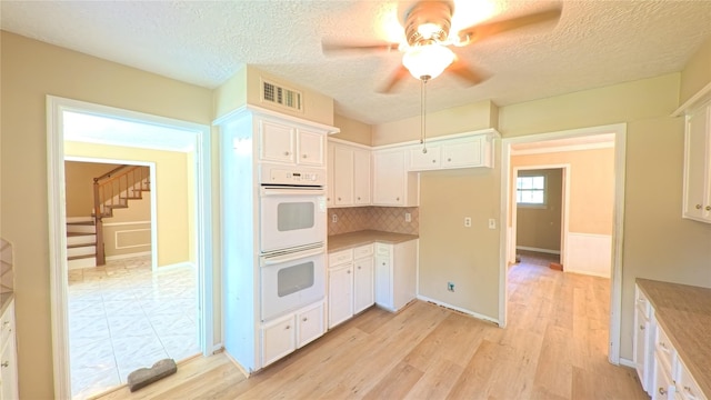 kitchen with decorative backsplash, a ceiling fan, light wood-type flooring, white double oven, and white cabinetry
