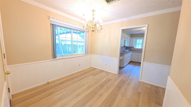 empty room featuring crown molding, an inviting chandelier, a textured ceiling, light wood-style flooring, and a wainscoted wall