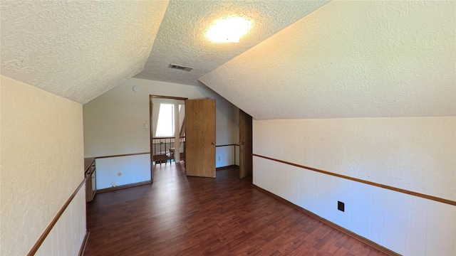 bonus room with a textured wall, a textured ceiling, a wainscoted wall, dark wood-type flooring, and vaulted ceiling