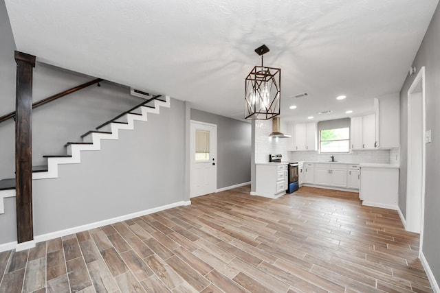 kitchen with baseboards, wall chimney range hood, light countertops, white cabinetry, and range with electric cooktop