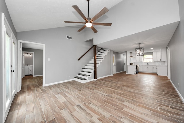 unfurnished living room featuring visible vents, baseboards, ceiling fan with notable chandelier, light wood finished floors, and stairs