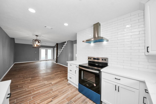 kitchen featuring baseboards, wall chimney range hood, light countertops, stainless steel electric range, and backsplash