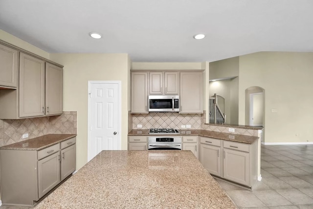 6315 Bain Dr, Missouri City, TX 77459 - kitchen with decorative backsplash, a peninsula, arched walkways, light tile patterned floors, and stainless steel appliances