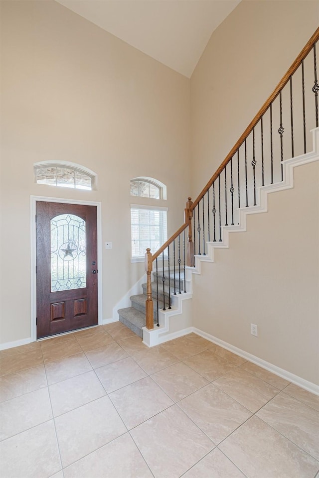 entrance foyer featuring stairs, light tile patterned flooring, high vaulted ceiling, and baseboards