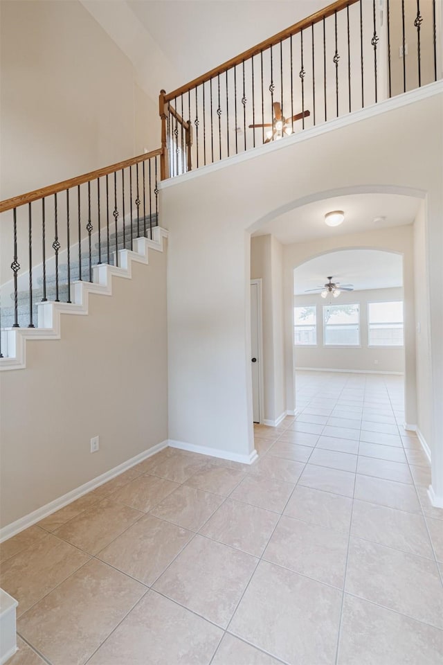 stairs with tile patterned flooring, a ceiling fan, a towering ceiling, baseboards, and arched walkways