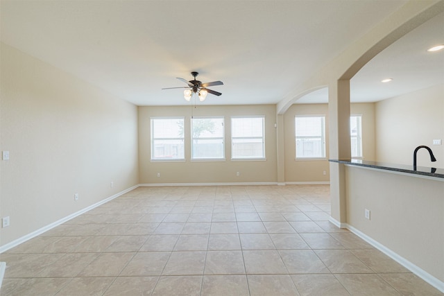 unfurnished room with baseboards, a ceiling fan, arched walkways, and light tile patterned flooring