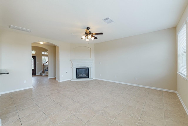unfurnished living room featuring light tile patterned flooring, a ceiling fan, visible vents, and a wealth of natural light