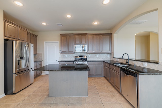 kitchen featuring a sink, arched walkways, stainless steel appliances, backsplash, and a kitchen island