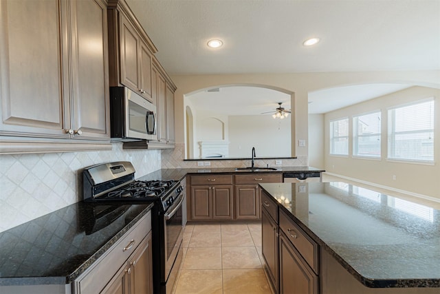 kitchen featuring ceiling fan, arched walkways, tasteful backsplash, a sink, and stainless steel appliances