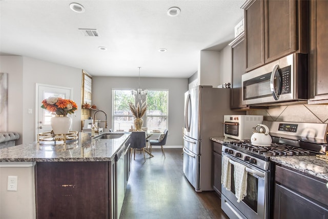 kitchen with dark brown cabinetry, a sink, an island with sink, stainless steel appliances, and visible vents