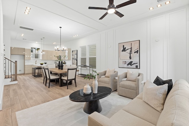 living area with visible vents, light wood-style flooring, stairway, and ceiling fan with notable chandelier