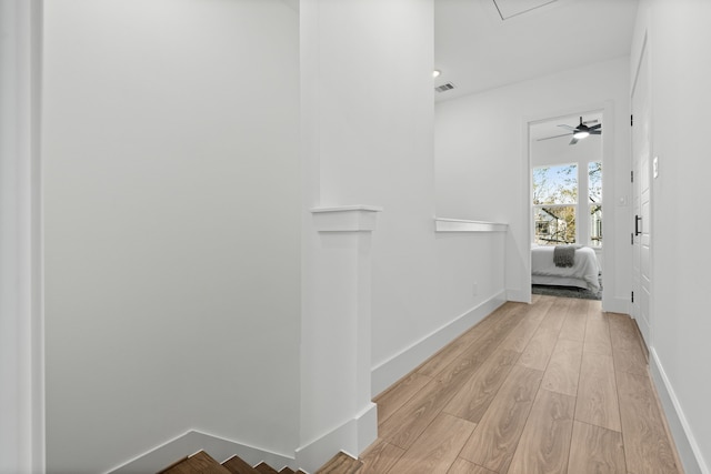 corridor with baseboards, attic access, light wood-style flooring, and an upstairs landing