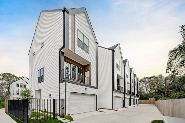 view of property exterior with a garage, fence, a balcony, and driveway