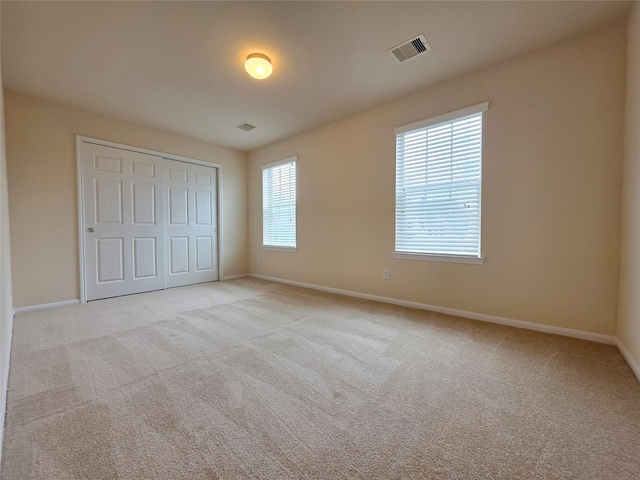 unfurnished bedroom with baseboards, visible vents, light carpet, and a closet