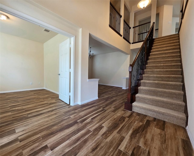 stairs featuring baseboards, visible vents, wood finished floors, and a high ceiling