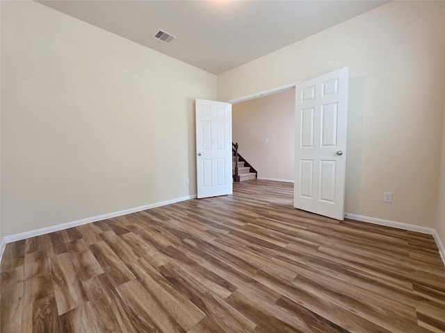 spare room featuring baseboards, stairs, wood finished floors, and visible vents