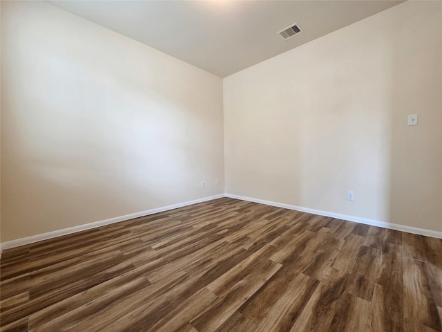 unfurnished room featuring baseboards, dark wood-style flooring, and visible vents