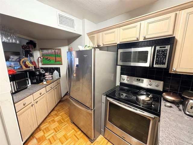 kitchen with visible vents, a textured ceiling, cream cabinets, appliances with stainless steel finishes, and backsplash