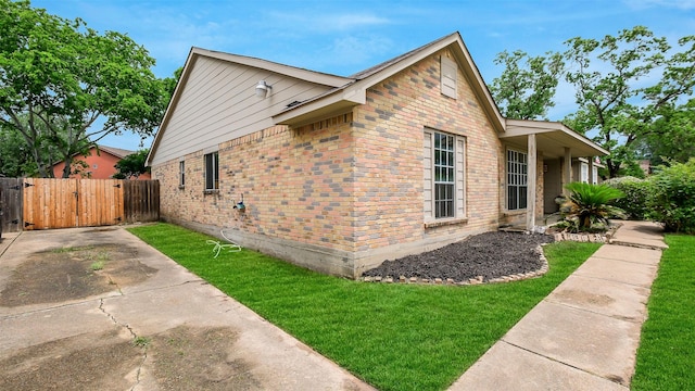 view of property exterior featuring brick siding, a gate, fence, and a yard