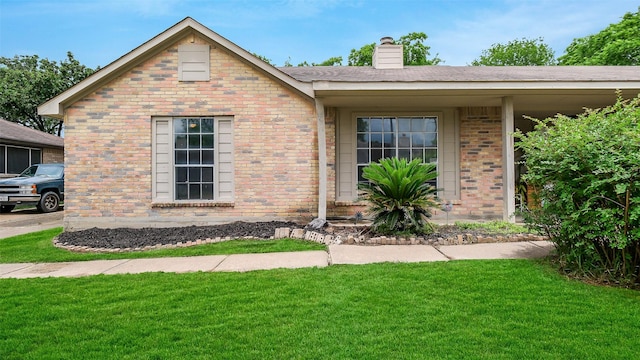 view of front facade with brick siding, a chimney, and a front lawn