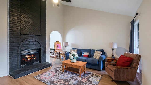 living room featuring a brick fireplace, ceiling fan, wood finished floors, and high vaulted ceiling
