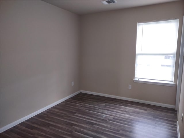 spare room featuring baseboards, dark wood-style flooring, and visible vents