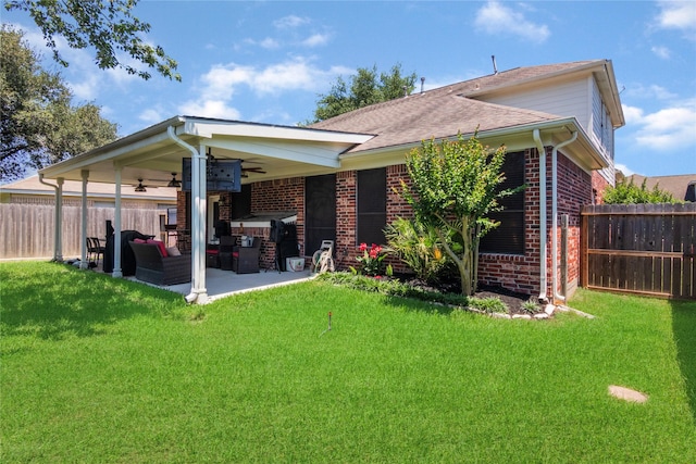rear view of property featuring ceiling fan, fence, brick siding, and a lawn