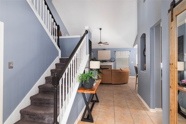 stairway with a ceiling fan, baseboards, tile patterned flooring, high vaulted ceiling, and a fireplace