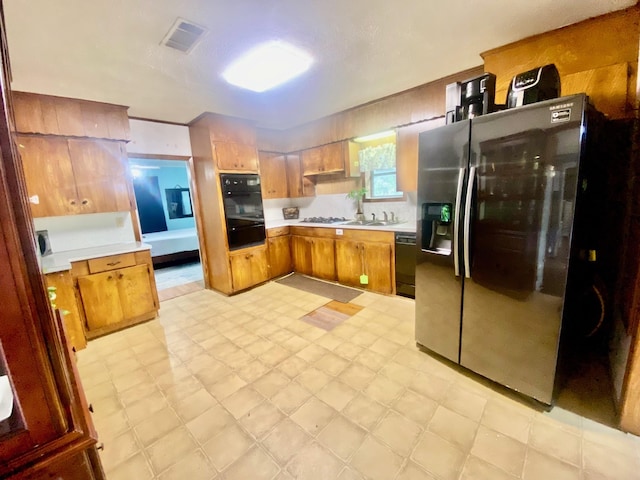 kitchen with light countertops, a warming drawer, black appliances, and brown cabinets